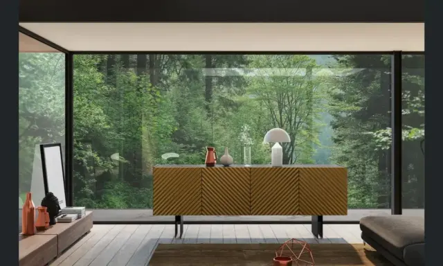 Madia moderna con ante a righe diagonali, un tavolino basso con oggetti decorativi e una grande vetrata su una foresta lussureggiante.
