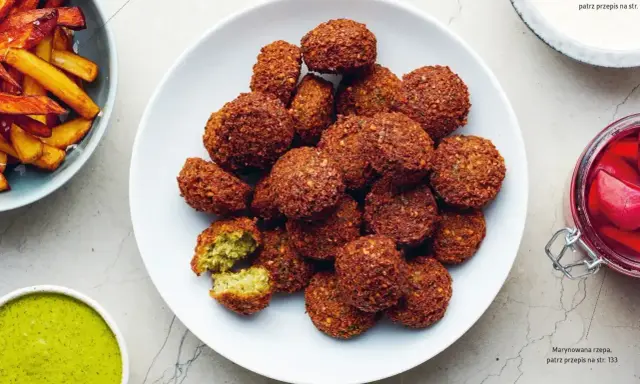 Talerz pełen chrupiących kuleczek, które są idealnym przykładem tego, co to jest falafel. Podane z zielonym sosem i frytkami.