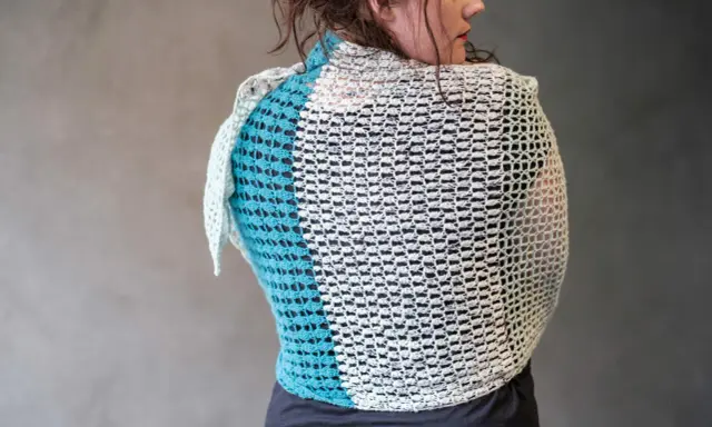 Mujer de espaldas con un cubre hombros a crochet de dos colores, blanco y azul turquesa, con un diseño calado.
