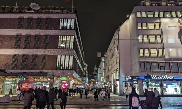 En livlig stockholm shopping street på kvällen. Folk promenerar förbi Åhléns City och Ur & Penn.