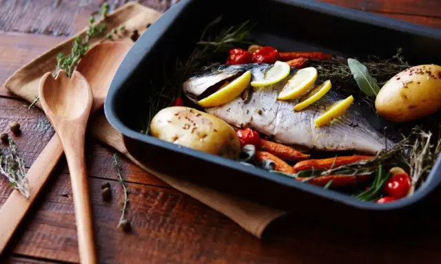 Pescado al horno con patatas, zanahorias y tomates, listo para servir.