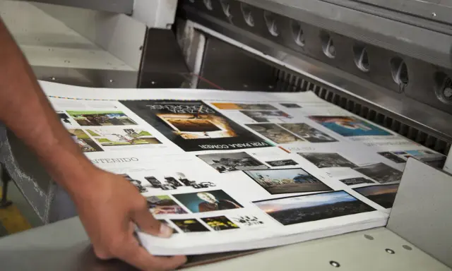 Mani che sistemano fogli stampati su una macchina da taglio, parte della post produzione di una rivista.