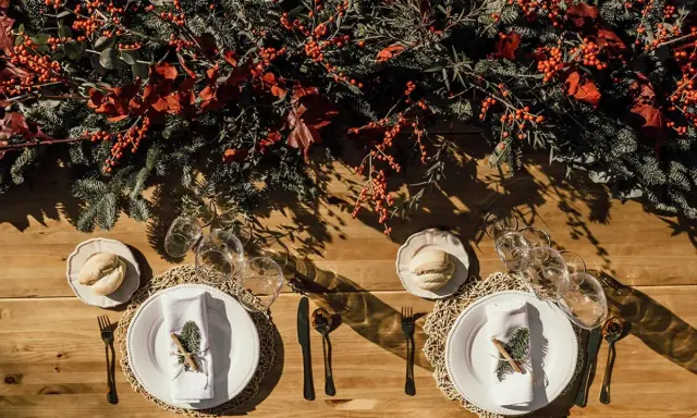 Decoración festiva para una boda en diciembre. Mesa de madera con ramas de pino, bayas rojas y detalles rústicos.