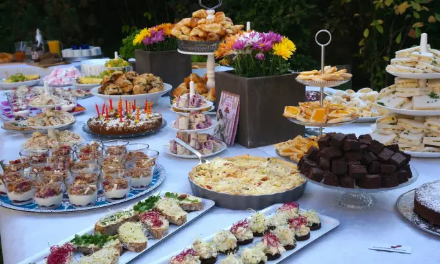 Ein üppiges Brunch Buffet im Freien mit Croissants, Quiche, Brownies, Sandwiches und süßen Leckereien.