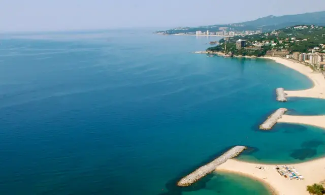 Bucht mit Wellenbrechern und Sandstränden in Calonge, Spanien. Die Küstenstadt erstreckt sich entlang des blauen Meeres.