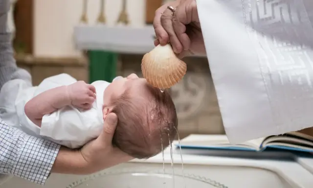 Chrzest dziecka. Kapłan polewa główkę niemowlęcia wodą święconą z muszli. To ważny moment, jak ile daje się na chrzciny.