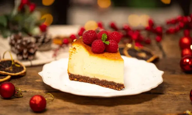 Sernik creme brulee z malinami i miętą, udekorowany na drewnianym stole, w świątecznej scenerii.