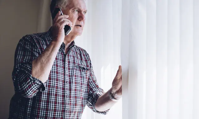 Zaniepokojony starszy mężczyzna rozmawia przez telefon, szukając informacji, gdzie zgłosić zaniedbywanie osoby starszej.