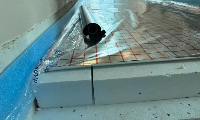 Układanie styropianu pod wylewkę. Warstwa izolacji z folią aluminiową i taśmą brzegową.