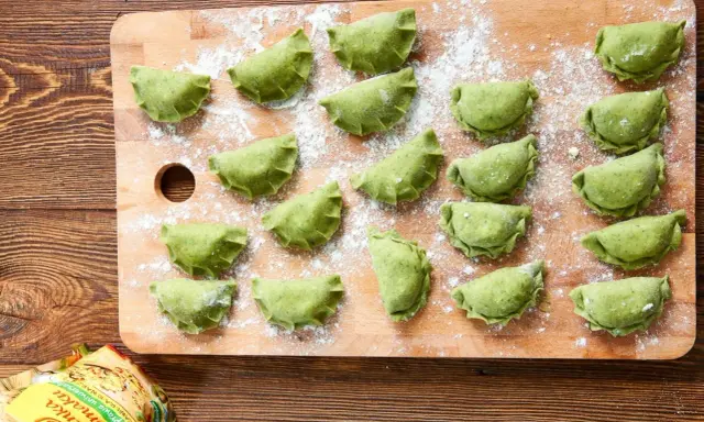 Zielone pierogi ze szpinakiem ułożone na desce, posypane mąką. Czekają na gotowanie.