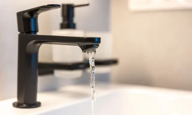 Robinet noir moderne, eau claire coulant dans un lavabo. Un adoucisseur d'eau est peut-être installé pour lutter contre l'eau calcaire.