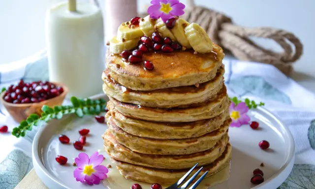 Pile de pancakes banane, garnie de fruits rouges, de rondelles de banane et de fleurs roses. Un délice pour le petit-déjeuner.