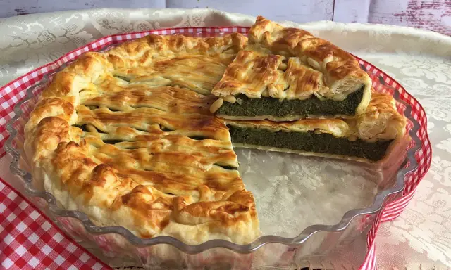 Torta salata ricotta e spinaci dorata e invitante, con una fetta tagliata che mostra il ripieno verde e cremoso.