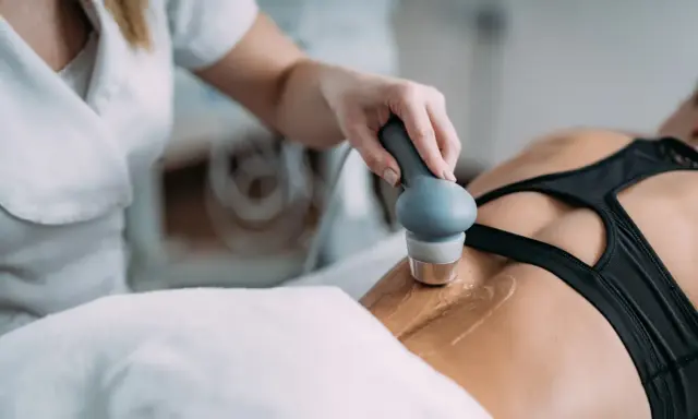 Fizjoterapeuta stosuje głowicę do terapii ultradźwiękami na plecy pacjentki, wspomagając regenerację.