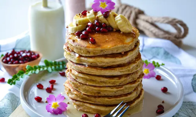 Pile de pancakes healthy garnis de bananes, grenades et fleurs roses. Un délice pour un petit-déjeuner sain.