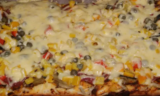 Pyszna pizza na grubym cieście z warzywami i roztopionym serem.
