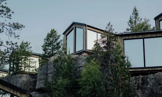 Moderna trähus med stora fönster klättrar uppför en stenig sluttning, omgivna av tallar. En idyllisk camping Lapland resort.