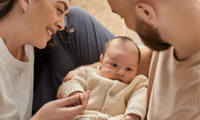 Una madre sonríe a su bebé, mientras el padre lo abraza. A pesar de que mi bebé no tiene apego conmigo, la familia se ve unida.