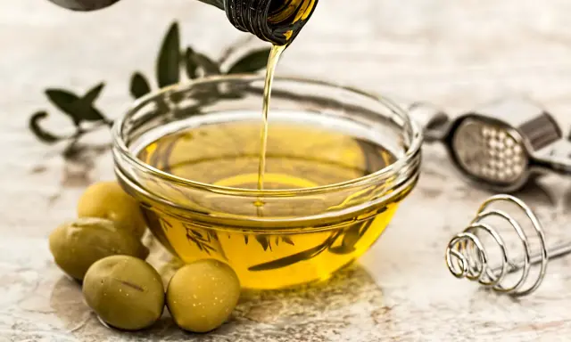 Aceite de oliva virgen extra vertiéndose en un cuenco, con aceitunas y utensilios de cocina. Sus características lo hacen ideal.
