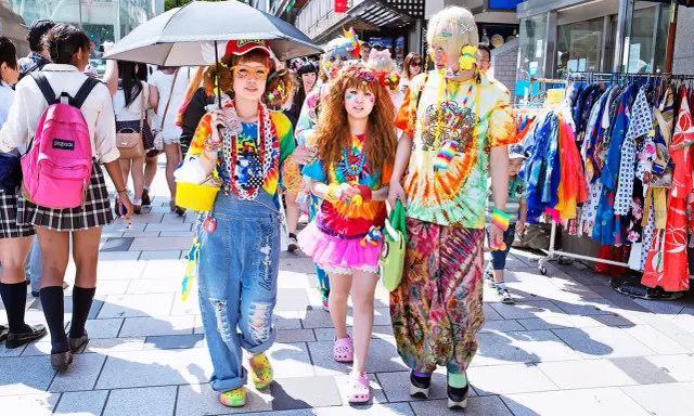 Kolorowy tłum w stylu harajuku, z tęczowymi ubraniami, dżinsowymi ogrodniczkami i jaskrawymi dodatkami, spaceruje ulicą.