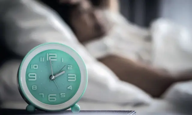 Ein Wecker neben einer schlafenden Person. Die Zeit ist kurz vor 2 Uhr. Ein Symbol für den zirkadianen Rhythmus.