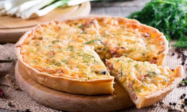 Pyszna tarta z porem i boczkiem, posypana serem i koperkiem, z kawałkiem już wyjętym.