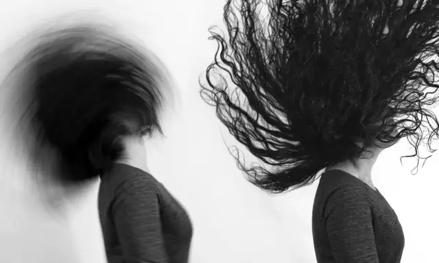 Dos cabezas con cabello largo y oscuro en movimiento, capturadas con un obturador fotográfico que crea un efecto de desenfoque dinámico.