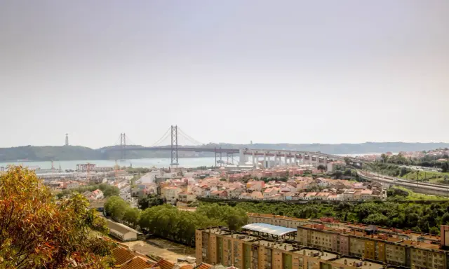 Blick auf Lissabon mit der Hängebrücke und dem Cristo Rei Denkmal. Im Vordergrund die Dächer von Häusern, die an den "Cemitério dos Prazeres" erinnern.