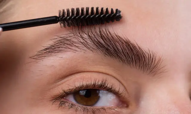 Une brosse à cils peigne les sourcils d'une femme pour les mettre en forme.