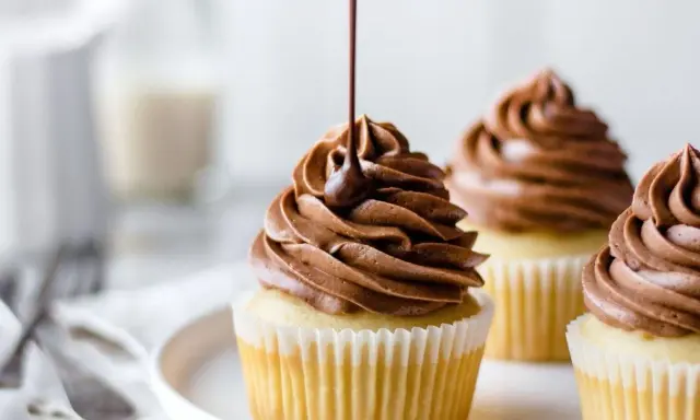 Glaçage onctueux de ganache montée mascarpone sur des cupcakes. Un filet de chocolat coule sur le glaçage.