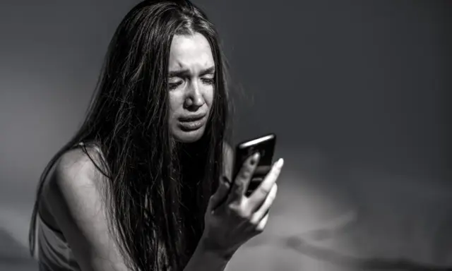 Ragazza piange guardando il telefono, vittima di revenge porn. La legge punisce chi diffonde immagini private senza consenso.