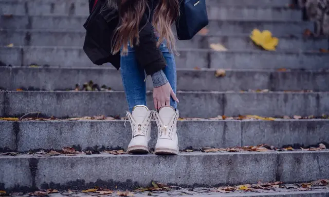 Kobieta w beżowych botkach na schodach, otoczona jesiennymi liśćmi.