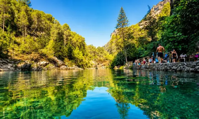 Un refrescante charco del aceite, rodeado de vegetación exuberante y rocas, con gente disfrutando del día.