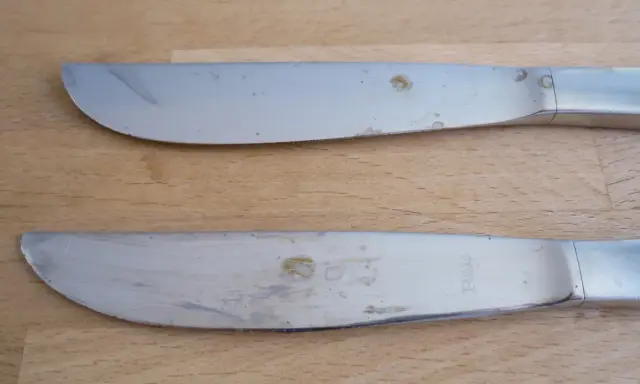 Zwei Messer mit deutlichen Rostflecken auf dem Besteck liegen auf einem Holztisch.