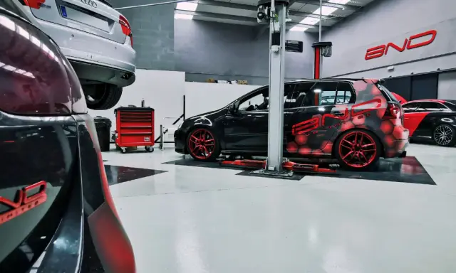Taller con coches modificados. Uno negro con diseño de hexágonos rojos y llantas rojas, otro negro y rojo con alerón. Se pregunta cuánto cuesta reprogramar un coche.