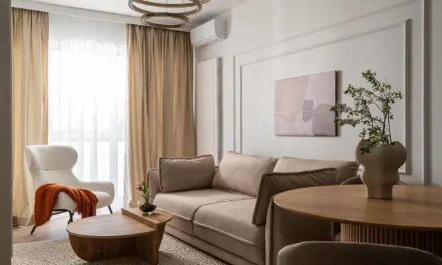 Nowoczesny salon szaro beżowy z wygodną kanapą, puszystym fotelem i drewnianymi meblami.
