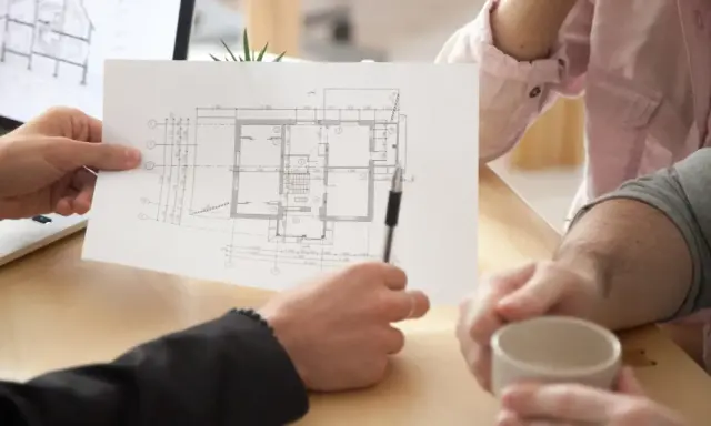 Architekt omawia z klientami projekt domu, wskazując na planowaną powierzchnię netto budynku.