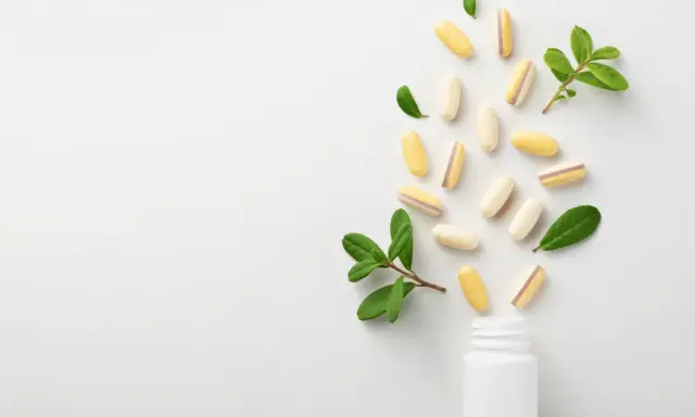 Kapsułki z lactobacillus plantarum rozsypują się z białej buteleczki, otoczone zielonymi listkami.