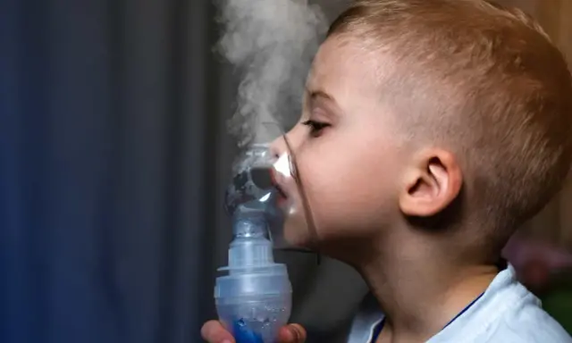 Chłopiec z maską inhalacyjną na twarzy, wdycha parę. Skuteczna inhalacja na katar u dziecka.
