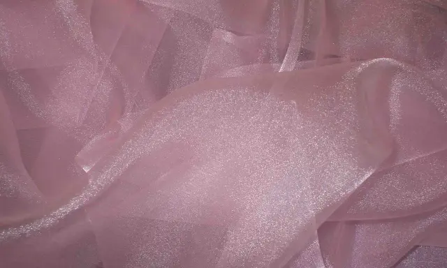 A shimmering pink organza fabric, with its sheer, crisp texture, drapes elegantly, catching the light.