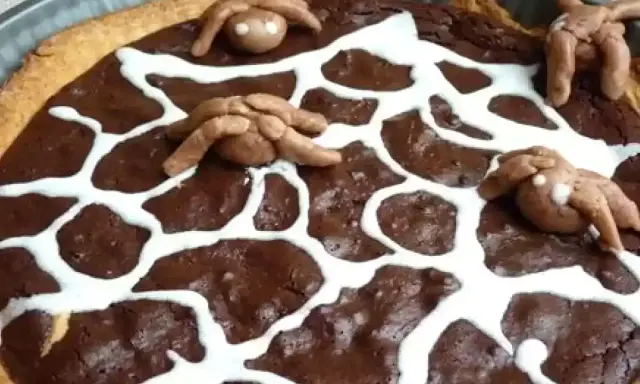 Tarte au chocolat d'Halloween décorée d'une toile d'araignée en glaçage blanc et d'araignées en pâte d'amande.