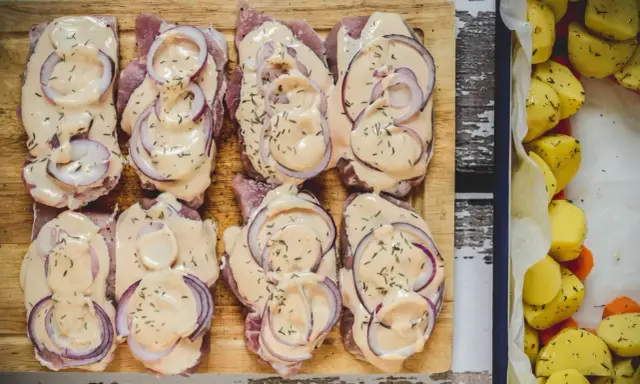 Schab pieczony w plastrach, polany kremowym sosem i posypany ziołami, obok pieczone ziemniaki.