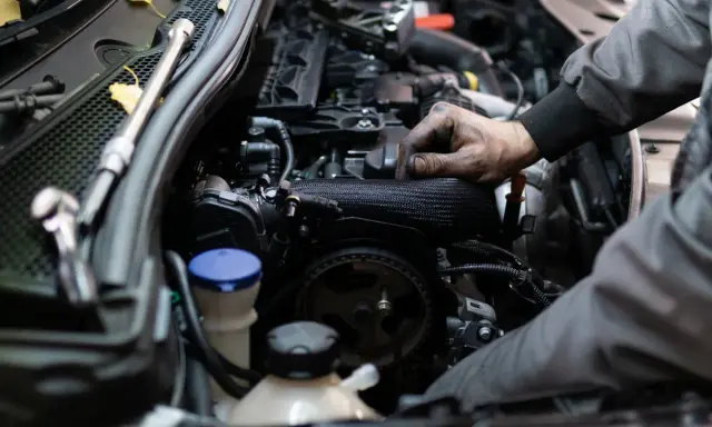 Mechanik pracuje przy silniku benzynowym, jego ręce są ubrudzone smarem.