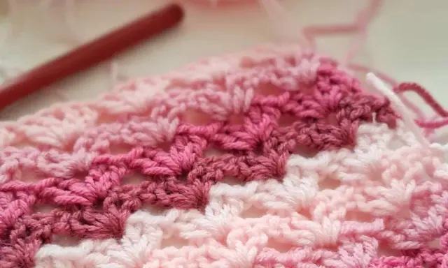 Tejido a crochet con hilo rosa y blanco. Un patrón de chaleco fácil en progreso, con un ganchillo rojo al fondo.
