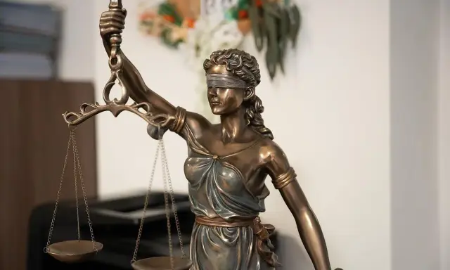 Estatua de la Justicia con venda y balanza, símbolo de imparcialidad. El texto "250.2 lec." aparece sutilmente.