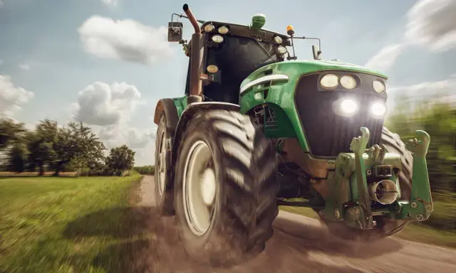 Zielony traktor pędzi po polnej drodze, gotowy do pracy. To maszyna rolnicza, której zakup jest ważną umową kupna sprzedaży.