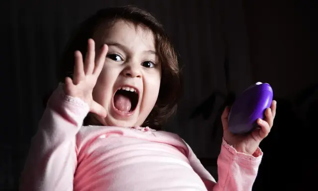 Niño asustado grita con la boca abierta, levantando una mano y sosteniendo un objeto morado.