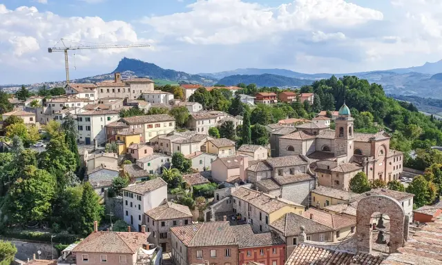 Un borgo pittoresco sulle colline riminesi, con tetti rossi, una chiesa con campanile e un paesaggio verdeggiante sullo sfondo.
