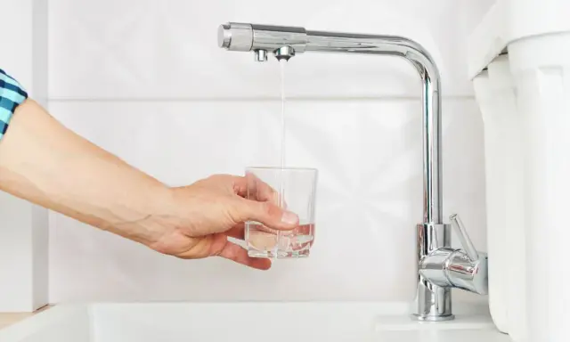 Main tenant rempli un verre d'eau sous un robinet de cuisine moderne, peut-être pour tester un nouveau joint mitigeur cuisine.