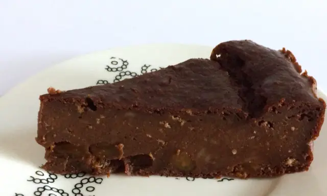 Una fetta di torta di pane al cioccolato, umida e ricca, con pezzi di frutta secca. La torta di pane ricetta della nonna, servita su un piatto bianco con decorazioni nere.